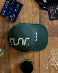 Green cap with 'runr' logo on a wooden surface with accessories.