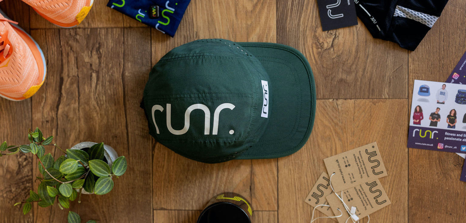 Green cap with 'runr' logo on a wooden surface with accessories.
